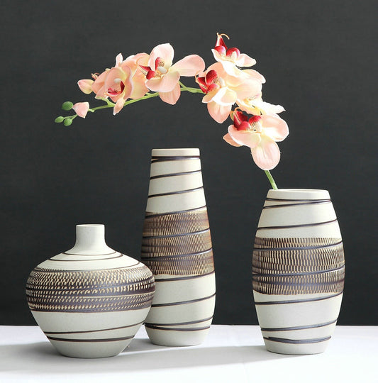 Set of three hand-textured ceramic vases in varying heights with striped pattern, styled with pink orchid stems on dark background
