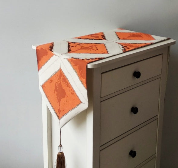 Geometric Patchwork Table Runner, cream fabric with bold orange panels and white intersecting lines with tassel detail