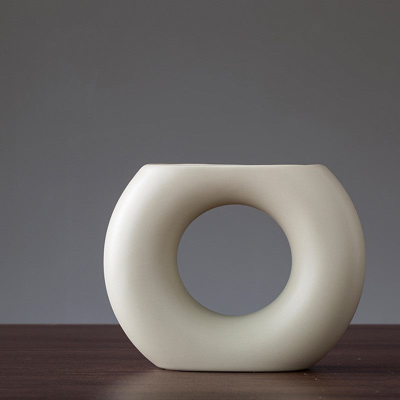 White ceramic vase with a circular design on a dark surface and gray background