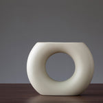 White ceramic vase with a circular design on a dark surface and gray background