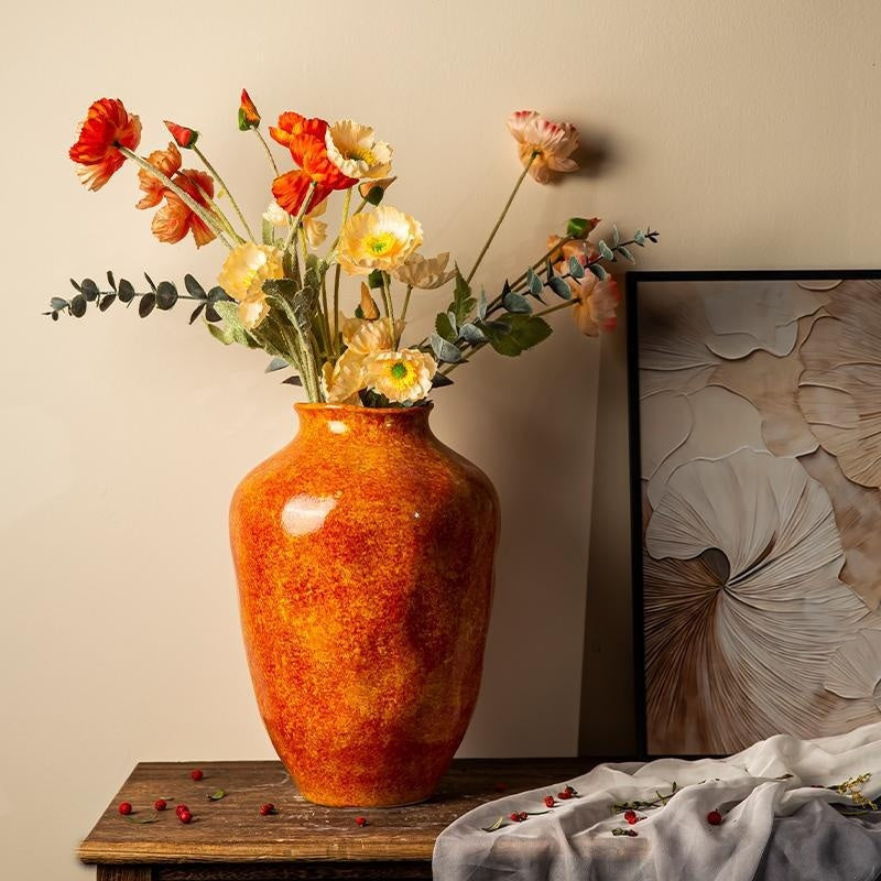 Decorative vase with flowers on a wooden table against a beige wall.