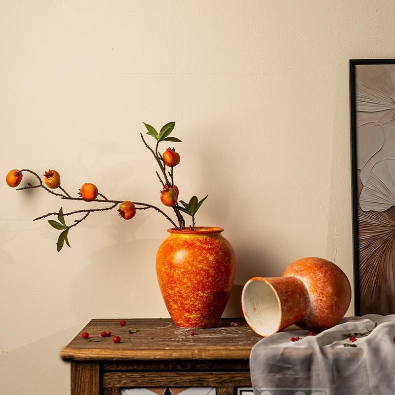 Decorative orange vase with branches on a wooden table against a beige wall.